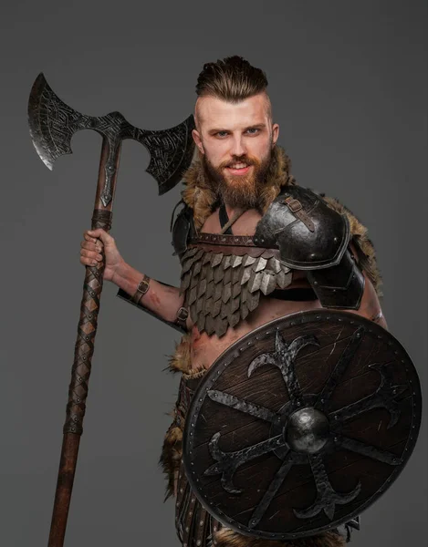 Intimidating bearded Viking wearing furs and light armor, gripping an axe on a gray background