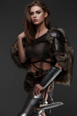 Zincir zırhlı ve kürklü çekici bir Viking temalı model, gri arka plana karşı bir balta tutuyor.