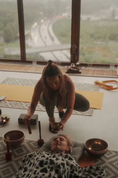 A peaceful scene of girls practicing spiritual activities and yoga using a singing Tibetan bowl, surrounded by a calming atmosphere in an apartment with a panoramic city view