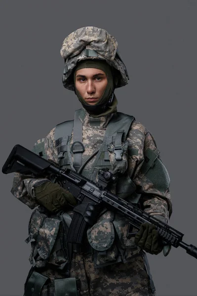 ユニフォームとヘルメットの若い兵士は 明白な灰色の背景に深刻な表現をポーズし 軍人の強さと献身を示しています — ストック写真