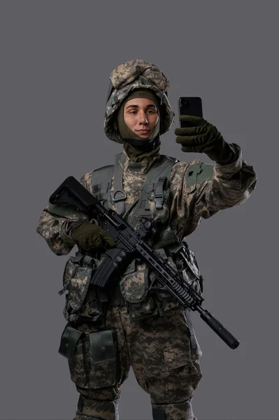 Military man with a gun and a mobile phone takes a selfie or has a video chat, showing a casual and modern side of a soldiers life