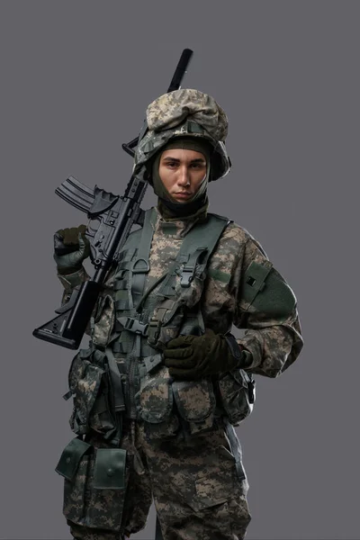 若い兵士は明白な灰色の背景に深刻な表現をポーズし 軍人の強さと献身を示しています — ストック写真