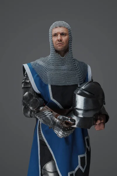 中世の鎧と青のサーコートを身に着けているロイヤルガード チェーンメールコイフ付き 手にヘルメットを保持立って 灰色の背景を背景に — ストック写真