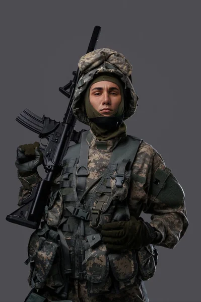 Young soldier in uniform and helmet poses with a serious expression on a plain grey background, showcasing the strength and dedication of military personnel
