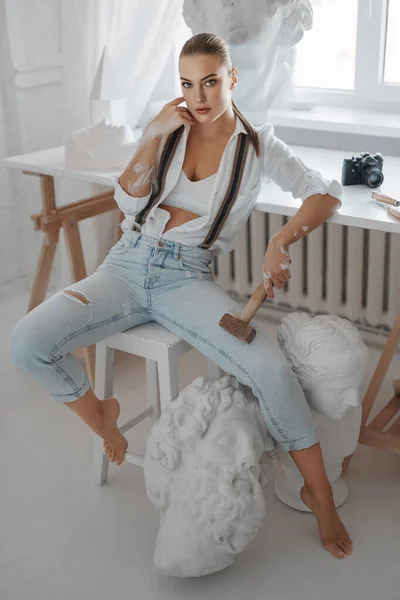 Atrakcyjna Rzeźbiarka Ubrana Luźną Białą Koszulę Dżinsy Szelkami Siedząca Stołku — Zdjęcie stockowe