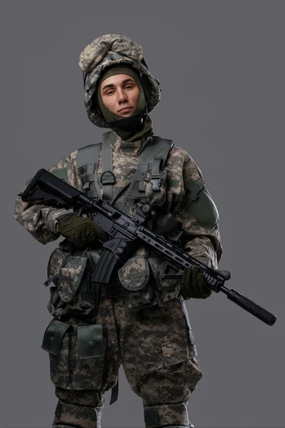 軍服とヘルメットの若者が灰色の背景にライフルを持っている — ストック写真