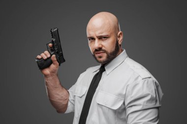 Gıcır gıcır beyaz giysili güçlü sakallı şahıs silahını hazırlıyor, bu da güvenlik veya dedektif rollerini öneriyor.