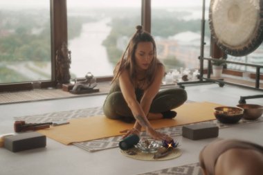 Spor giyimli bir kadın, arka planda panoramik bir şehir manzarası olan bir apartman dairesinde yoga yapıyor.