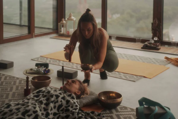 A peaceful scene of girls practicing spiritual activities and yoga using a singing Tibetan bowl, surrounded by a calming atmosphere in an apartment with a panoramic city view