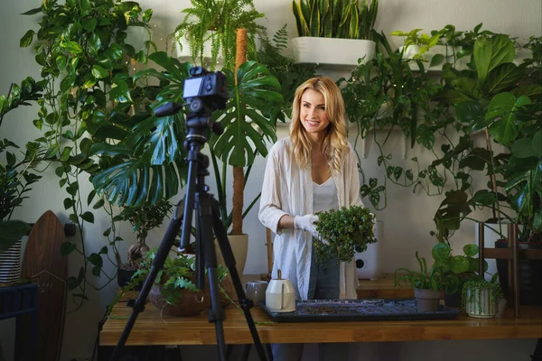 Stylish florist and blogger capturing her plant care routine in room with vibrant greenery