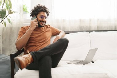 Akıllı telefonunun yanında dizüstü bilgisayarı olan neşeli bir Hintli, sade bir atmosferde pozitiflik yayıyor.