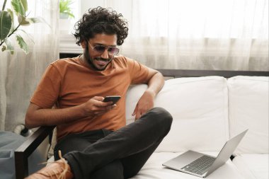 Gülümseyen neşeli bir öğrenci. Akıllı telefon kullanıyor. Yanında dizüstü bilgisayar var.