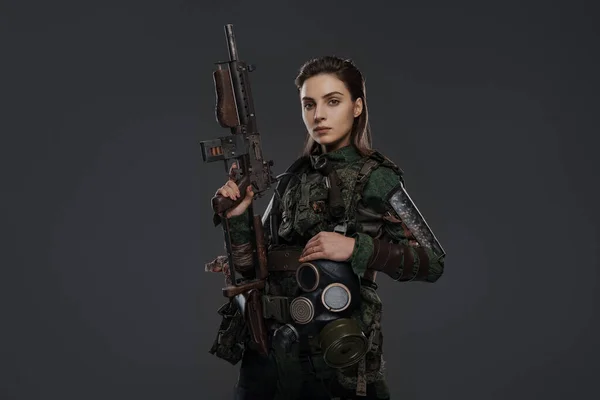 Portrait of a female soldier in military attire, holding a homemade automatic rifle, depicting a rebel or partisan in a Middle Eastern conflict against a gray background