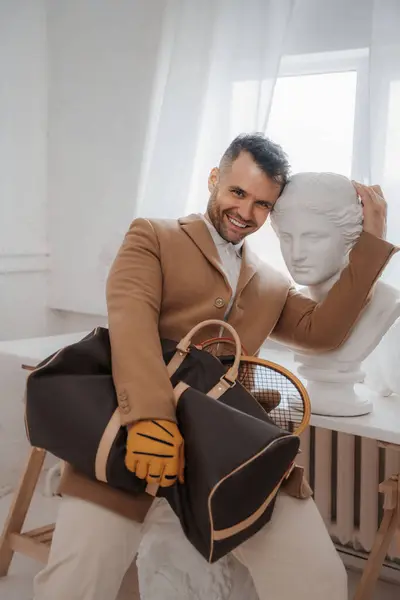 在古希腊雕塑工作室里 一个迷人 面带微笑的男人拿着一个包和网球拍 非常迷人 — 图库照片