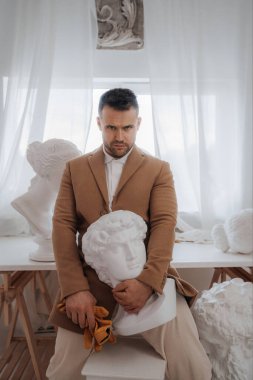 Eski para tarzında zengin bir adam, heykeltıraşların atölyesindeki antik Yunan heykelleriyle çevrili.