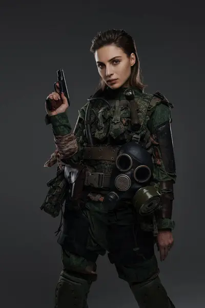 Portrait of a female soldier in military uniform with a pistol, embodying a rebel or partisan in a Middle Eastern conflict against a gray backdrop