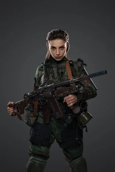 Portrait of a female soldier in military attire, holding a homemade automatic rifle, depicting a rebel or partisan in a Middle Eastern conflict against a gray background