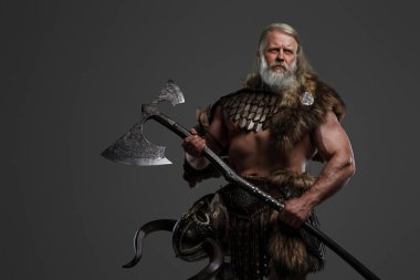 Eski Viking savaşçısı, gri saçlı ve sakallı, kürk ve hafif zırhlı, tarafsız bir arkaplana karşı iki elli bir balta kullanıyor.