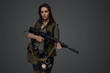 Hayatta kalma kıyafeti giymiş, gri bir arka plana karşı tüfekle poz veren Orta Doğulu bir kadın, dayanıklılık ve dayanıklılık tasvir ediyor.