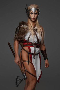Fantezi zırhlı kaslı sarışın bir Viking kadın gri arka planda iki balta tutuyor.