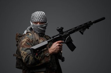 Orta Doğulu bir militan, beyaz keffiyeh giyip kamufle olmuş, otomatik bir tüfeği var, tarafsız gri bir zemine dayanıyor.