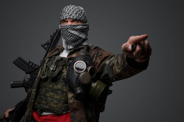 Orta Doğu radikal fanatik askeri, beyaz keffiyeh giymiş ve kamufle olmuş bir üniforma giymiş, tüfekle silahlanmış, parmağını gri arka planda tehditkar bir şekilde işaret ediyor.