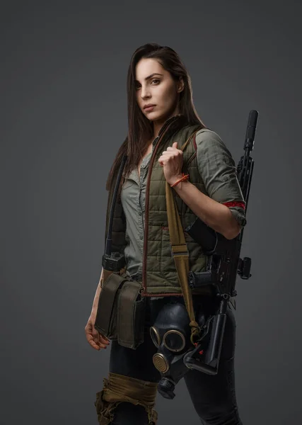 Woman in post-apocalyptic survival clothing, this photo showcases her strength as she confidently holds an assault rifle against a gray background