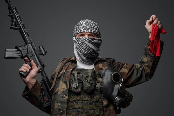 Ближневосточный солдат-фанатик радикалов, одетый в белую кеффию и камуфляжную полевую форму, вооруженный винтовкой, поднял руку, держа красную тряпку и пульт дистанционного управления