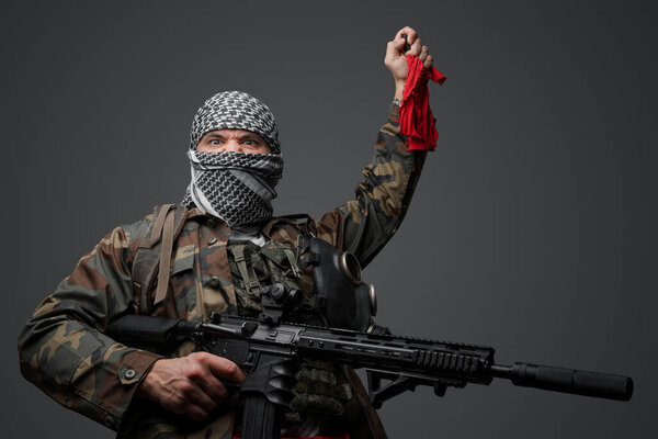 Ближневосточный солдат-фанатик радикалов, одетый в белую кеффию и камуфляжную полевую форму, вооруженный винтовкой, поднял руку, держа красную тряпку и пульт дистанционного управления