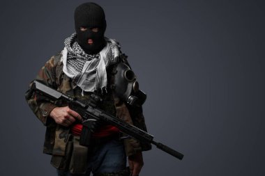Siyah kar maskesi ve kamuflajlı üniforma giyen, soğuk gri bir zemine karşı otomatik tüfekli bir Orta Doğulu radikal askerin portresi.