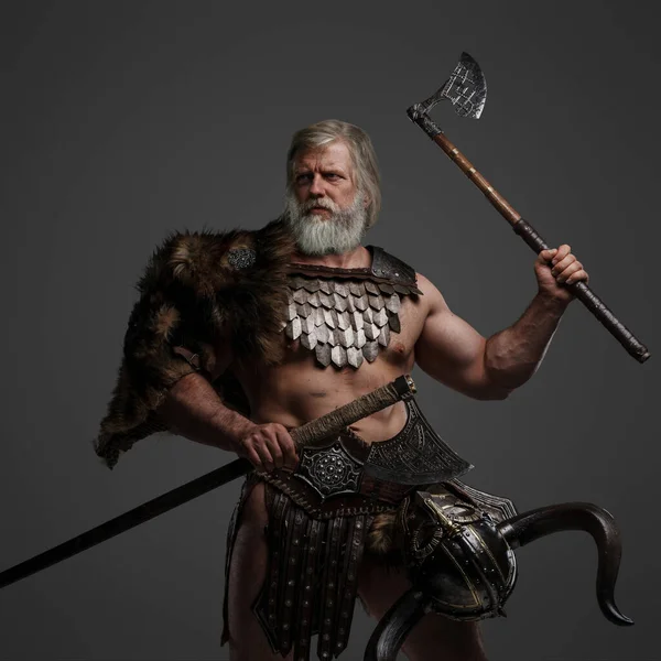 Grizzled elderly Viking warrior, displaying strength and wisdom, clad in furs and light armor, with a helmet slung on his waist, brandishing dual axes on a neutral background