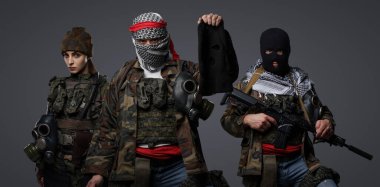 Üç Ortadoğulu militan grubu kamuflaj üniformaları, keffiyehler ve kar maskeleri giyip gri arka planda poz veriyorlar.