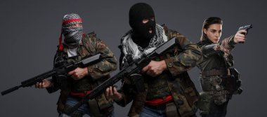 Üç Ortadoğulu militan grubu kamuflaj üniformaları, keffiyehler ve kar maskeleri giyip gri arka planda poz veriyorlar.
