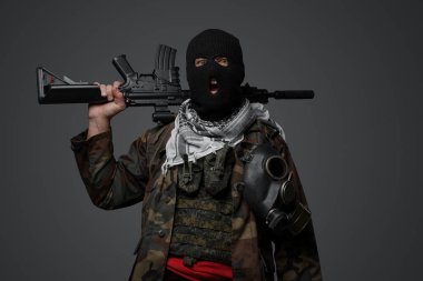 Orta Doğu 'dan radikal fanatik bir asker, siyah kar maskesi ve kamufle olmuş bir üniformayla gizlenmiş, otomatik tüfekli, gri bir arka planda.
