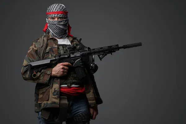 中東の急進的な狂信的な兵士が白いケフィエとカモフラッグのフィールドユニフォームを寄贈し 自動ライフルで武装し 灰色の背景に対して — ストック写真