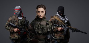 Üç Ortadoğulu militan grubu kamuflaj üniformaları, keffiyehler ve kar maskeleri giyip gri arka planda poz veriyorlar.