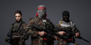 Üç Ortadoğulu militan grubu kamuflaj üniformaları, keffiyehler ve kar maskeleri giyip gri arka planda poz veriyorlar.