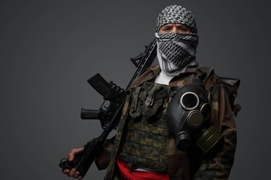 Orta Doğulu bir militan, beyaz keffiyeh giyip kamufle olmuş, otomatik bir tüfeği var, tarafsız gri bir zemine dayanıyor.