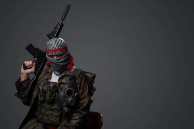 Orta Doğulu bir militan, beyaz keffiyeh giyip kamufle olmuş, otomatik bir tüfeği var, tarafsız gri bir zemine dayanıyor.