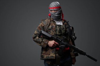 Orta Doğulu bir militan, beyaz keffiyeh giyip kamufle olmuş, otomatik bir tüfeği var, tarafsız gri bir zemine dayanıyor.