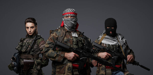 Группа из трех ближневосточных боевиков, одетых в камуфляжную форму, кеффиев и балаклавов, позирующих на сером фоне