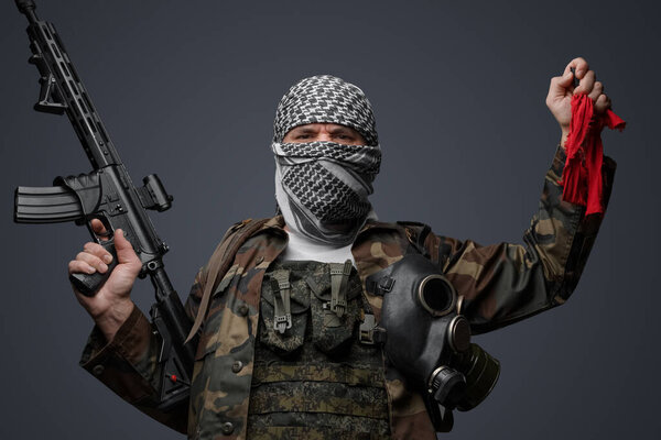 Ближневосточный солдат-фанатик радикалов, одетый в белую кеффию и камуфляжную полевую форму, вооруженный винтовкой, поднял руку, держа красную тряпку и пульт дистанционного управления
