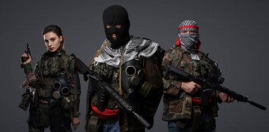 Üç Ortadoğulu militan grubu kamuflaj üniformaları, keffiyehler ve kar maskeleri giyip gri arka planda poz veriyorlar.