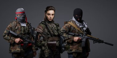 Üç Ortadoğulu militan grubu kamuflaj üniformaları, keffiyehler ve kar maskeleri giyip gri arka planda poz veriyorlar.