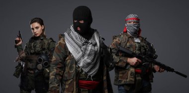 Orta Doğu 'dan radikal radikallerin üçlüsü kamuflaj, keffiyeh ve kar maskesi giyerek gri arka planda poz veriyorlar.