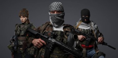 Üç Ortadoğulu militan grubu kamuflaj üniformaları, keffiyehler ve kar maskeleri giyip gri arka planda poz veriyorlar.