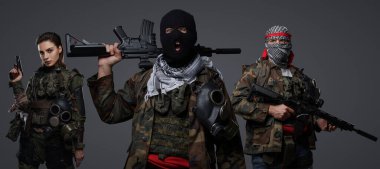 Üç Ortadoğulu militan grubu kamuflaj üniformaları, keffiyehler ve kar maskeleri giyip gri arka planda poz veriyorlar.
