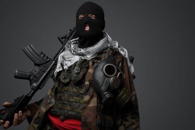 Orta Doğu 'dan radikal fanatik bir asker, siyah kar maskesi ve kamufle olmuş bir üniformayla gizlenmiş, otomatik tüfekli, gri bir arka planda.