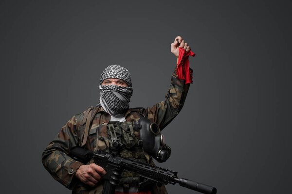 Ближневосточный солдат-фанатик радикалов, одетый в белую кеффию и камуфляжную полевую форму, вооруженный винтовкой, поднял руку, держа красную тряпку и пульт дистанционного управления