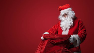 Noel Baba ağır bir çuval taşıyor, Noel hediyelerini teslim etmeye hazır.